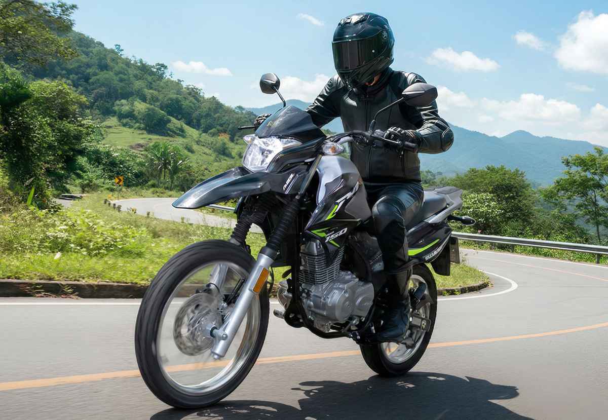 Motociclista conduciendo una Suzuki DR150, una de las motos más vendidas de Colombia, recorriendo una carretera asfaltada en un paisaje montañoso.