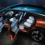 Toma cenital (vista desde arriba) con las puertas abiertas del nuevo monovolumen conceptual Renault R-Space Lab de color bronce metalizado. La imagen revela por completo el amplio habitáculo, destacando la inmensa pantalla panorámica openR que abarca el tablero, el compacto volante tipo yugo con dirección steer-by-wire y los tres asientos individuales traseros sobre un piso completamente plano. El techo de cristal continuo baña el interior con luz.