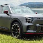 Vista de tres cuartos delantero de la SUV eléctrica premium Smart #5 en su versión deportiva Brabus. La carrocería luce un color Gris Atom Mate con líneas inferiores rojas, rines bitono de 21 pulgadas y faros LED. El vehículo está estacionado sobre el césped con un lago y montañas al fondo, luciendo una placa frontal con la inscripción #5.