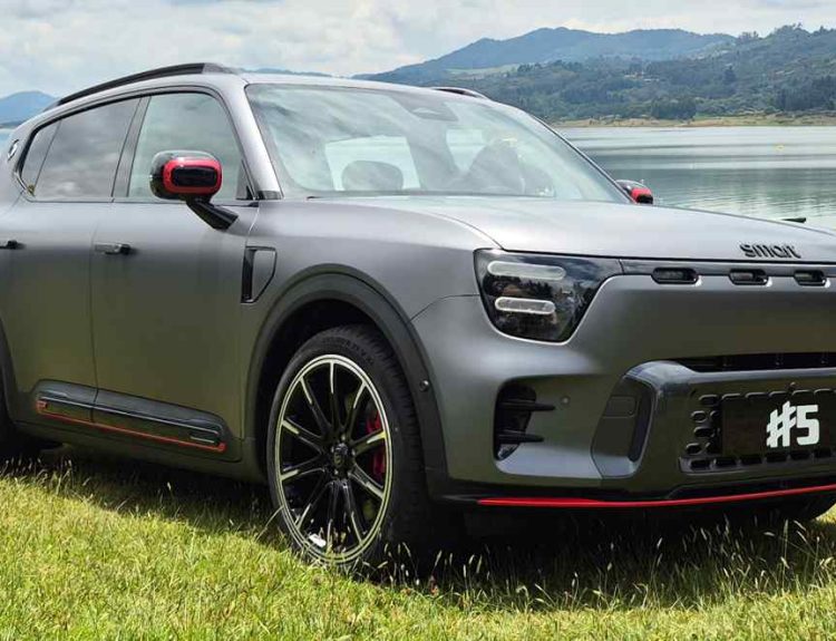 Vista de tres cuartos delantero de la SUV eléctrica premium Smart #5 en su versión deportiva Brabus. La carrocería luce un color Gris Atom Mate con líneas inferiores rojas, rines bitono de 21 pulgadas y faros LED. El vehículo está estacionado sobre el césped con un lago y montañas al fondo, luciendo una placa frontal con la inscripción #5.