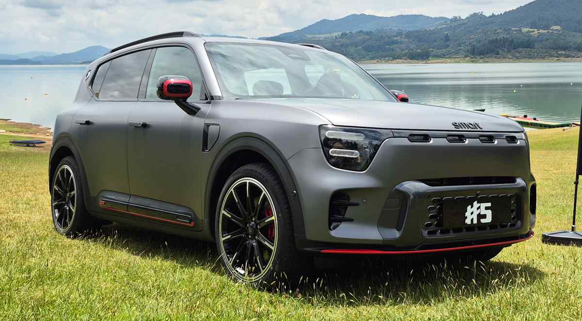Vista de tres cuartos delantero de la SUV eléctrica premium Smart #5 en su versión deportiva Brabus. La carrocería luce un color Gris Atom Mate con líneas inferiores rojas, rines bitono de 21 pulgadas y faros LED. El vehículo está estacionado sobre el césped con un lago y montañas al fondo, luciendo una placa frontal con la inscripción #5.