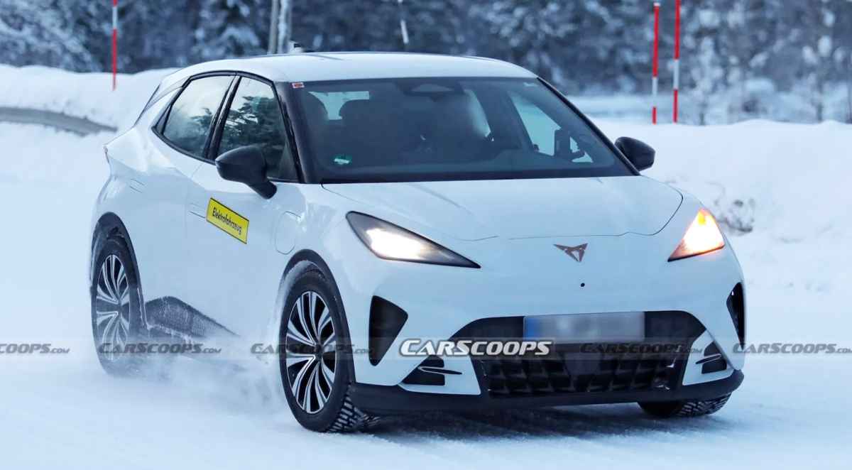 Fotografía espía del nuevo carro eléctrico Cupra Raval pintado en color blanco, circulando sin camuflaje por una carretera cubierta de nieve durante sus pruebas invernales. Se aprecia claramente su diseño frontal con faros LED estrechos, entradas de aire deportivas y el icónico logotipo cobrizo de Cupra en el capó.