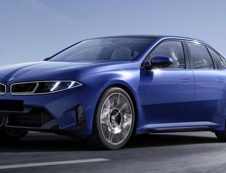 Vista frontal y lateral en movimiento del nuevo sedán eléctrico BMW i3 en color azul Le Castellet, recorriendo una carretera costera junto a montañas rocosas. Destaca su diseño frontal futurista con paneles luminosos integrados, rines aerodinámicos de 21 pulgadas y la silueta clásica deportiva de la Serie 3.