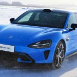 Vista frontal diagonal de un sedán eléctrico Xiaomi SU7 color azul brillante, con placa visible, en plena carrera sobre una pista de nieve a alta velocidad, demostrando su desempeño dinámico y tecnología de tracción en condiciones invernales.
