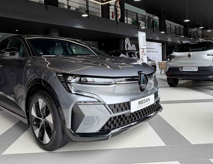 Una vista interior de ángulo bajo del renovado concesionario Renault Sanautos en Floridablanca, Santander, mostrando un sedán eléctrico Megane E-Tech plateado en primer plano y una SUV Kardian blanca al fondo, bajo moderna iluminación geométrica de LED, ilustrando el nuevo concepto de exhibición New'R y la inversión de $480 millones.
