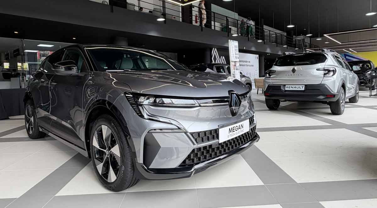 Una vista interior de ángulo bajo del renovado concesionario Renault Sanautos en Floridablanca, Santander, mostrando un sedán eléctrico Megane E-Tech plateado en primer plano y una SUV Kardian blanca al fondo, bajo moderna iluminación geométrica de LED, ilustrando el nuevo concepto de exhibición New'R y la inversión de $480 millones.