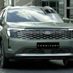 Vista frontal tres cuartos de la nueva Ford Territory Trend de color gris verdoso estacionada en una calle urbana moderna, destacando su parrilla y luces LED.