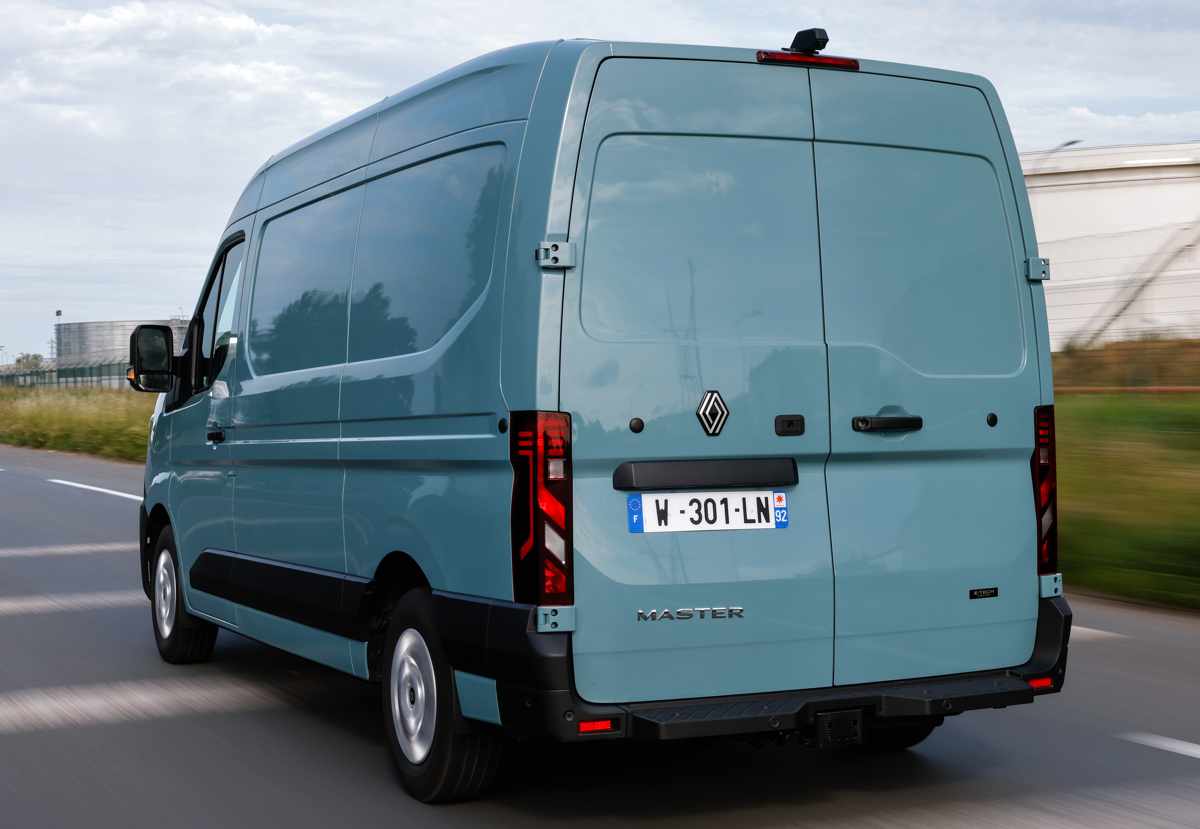 Vista trasera de tres cuartos de la furgoneta utilitaria Renault Master de nueva generación en color azul claro, captada en movimiento en la carretera, mostrando sus puertas traseras dobles y modernos pilotos LED verticales.