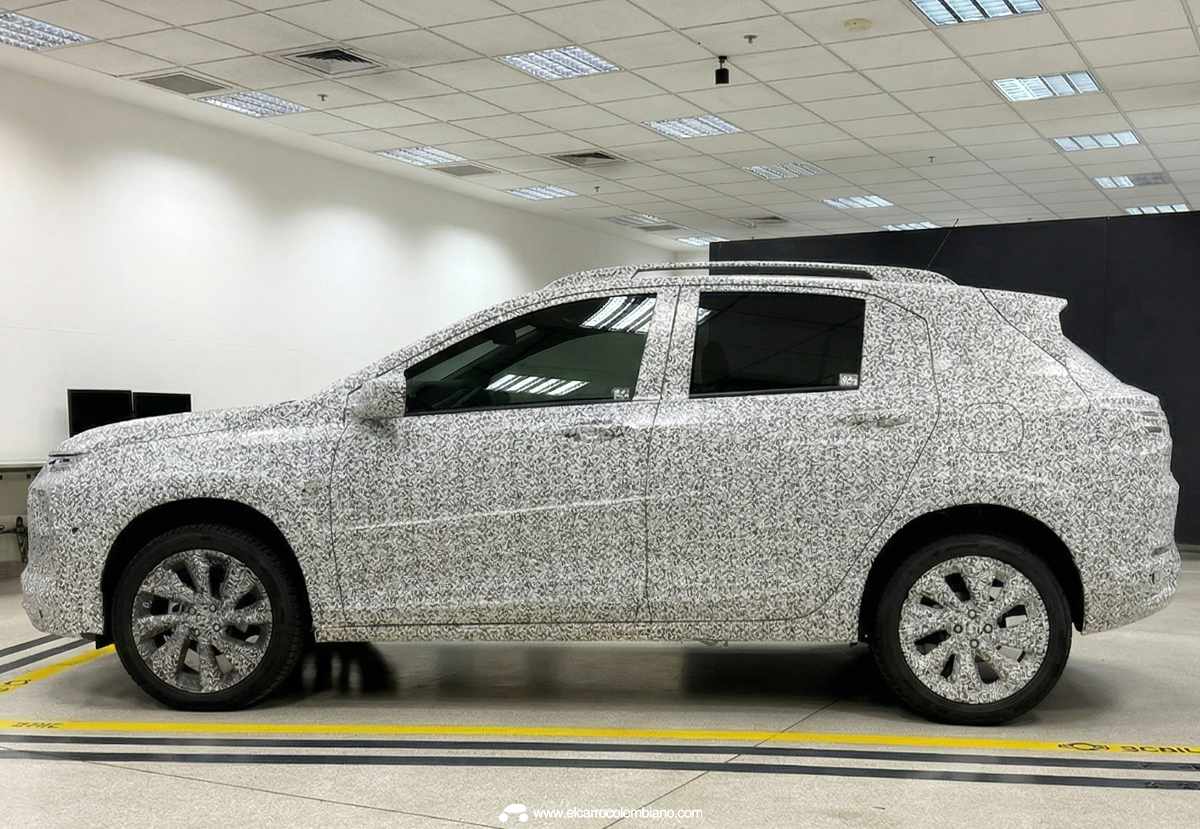 Perfil lateral completo del Chevrolet Sonic camuflado en el laboratorio, luciendo su silueta compacta, rines bitono y líneas laterales compartidas con el Onix HB.