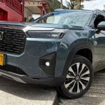 Un SUV Honda WR-V gris oscuro estacionado junto a una casa tradicional de paredes rojas en el eje cafetero de Colombia, luciendo placas amarillas de Colombia.