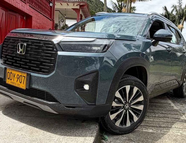 Un SUV Honda WR-V gris oscuro estacionado junto a una casa tradicional de paredes rojas en el eje cafetero de Colombia, luciendo placas amarillas de Colombia.