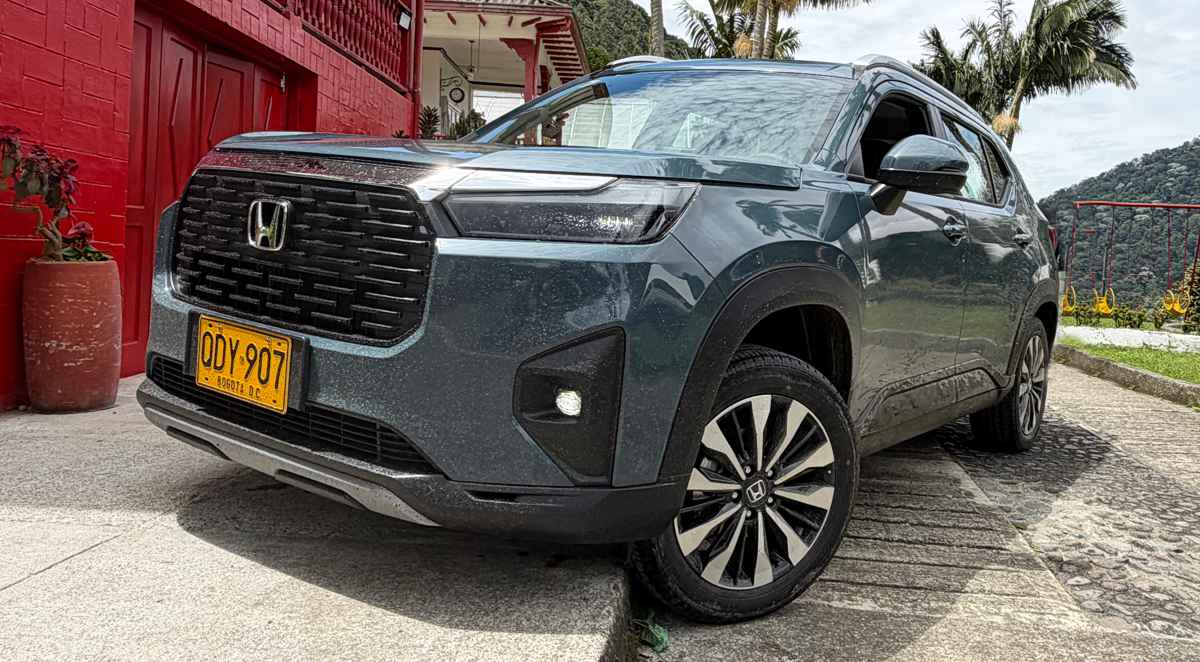 Un SUV Honda WR-V gris oscuro estacionado junto a una casa tradicional de paredes rojas en el eje cafetero de Colombia, luciendo placas amarillas de Colombia.