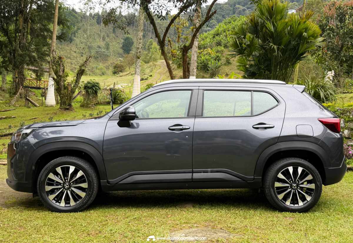 Vista de perfil lateral completo de la Honda WR-V gris oscura estacionada sobre grama en un paisaje verde de el Eje Cafetero, Colombia, resaltando las líneas de diseño del SUV.