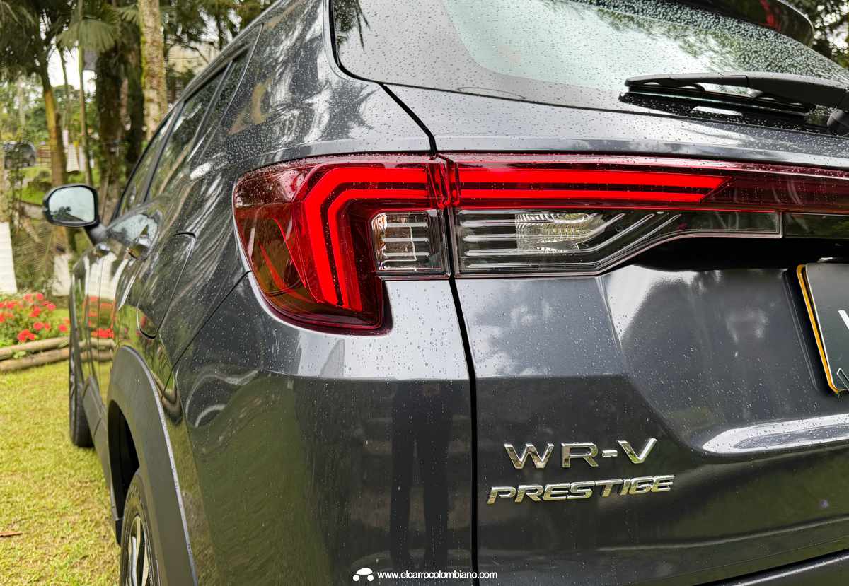 Vista trasera detallada de la Honda WR-V Prestige gris oscura en Colombia, estacionada sobre césped verde, con las luces LED encendidas y los emblemas 