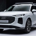 Vista de tres cuartos delantera de la nueva Audi Q3 SUV MHEV color blanco, estacionada en un estudio. Destaca su amplia parrilla frontal oscura y faros LED divididos, con barras de techo instaladas.