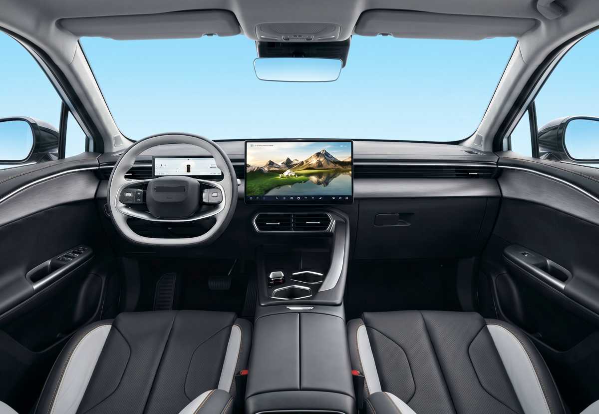 Vista frontal del interior y tablero de la Chery E5, mostrando el volante multifunción de dos radios, el gran panel de instrumentos digital y la pantalla táctil dual flotante panorámica. La consola central moderna incluye un cargador inalámbrico y selector de marchas rotativo. Los asientos tienen detalles en blanco y naranja.