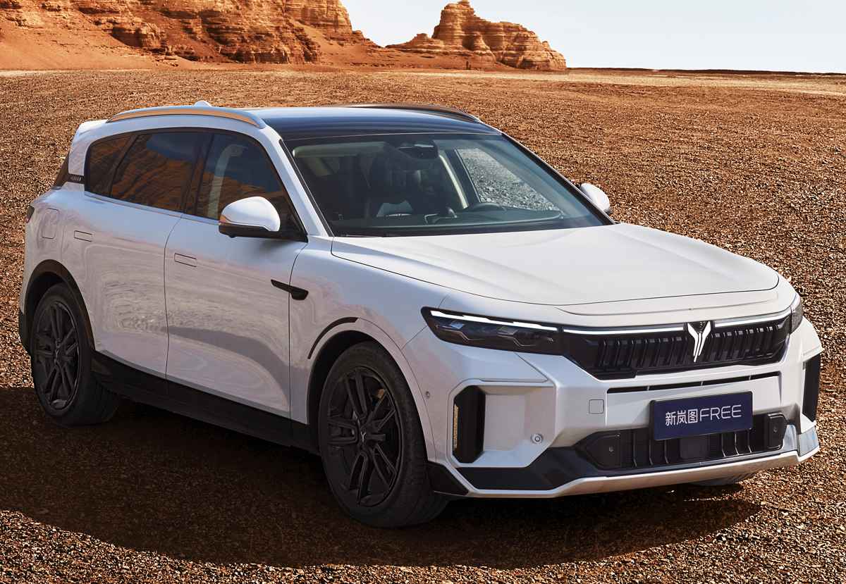 Vista frontal de tres cuartos de la Voyah Free 318 color blanco alpino, estacionada en un paisaje desértico rocoso bajo un cielo despejado. Resaltan sus rines oscuros y protectores de carrocería negros.