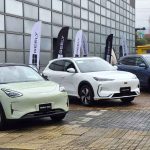 Vista frontal de la nueva línea de vehículos Geely durante su lanzamiento en Colombia. De izquierda a derecha: el city car eléctrico Geely EX2 verde claro, la SUV eléctrica Geely EX5 blanca y la SUV híbrida Geely Starray EM-i azul, estacionados junto a banderas de la marca.