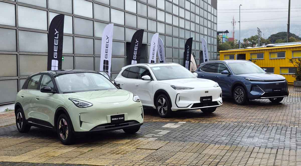 Vista frontal de la nueva línea de vehículos Geely durante su lanzamiento en Colombia. De izquierda a derecha: el city car eléctrico Geely EX2 verde claro, la SUV eléctrica Geely EX5 blanca y la SUV híbrida Geely Starray EM-i azul, estacionados junto a banderas de la marca.