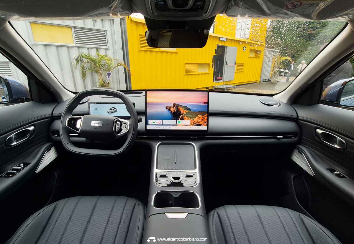 Vista frontal panorámica del interior y tablero de la nueva línea Geely. Muestra un diseño de cabina minimalista con volante multifunción de base plana, cuadro de instrumentos digital, gran pantalla táctil central flotante y consola con cargador inalámbrico dual.