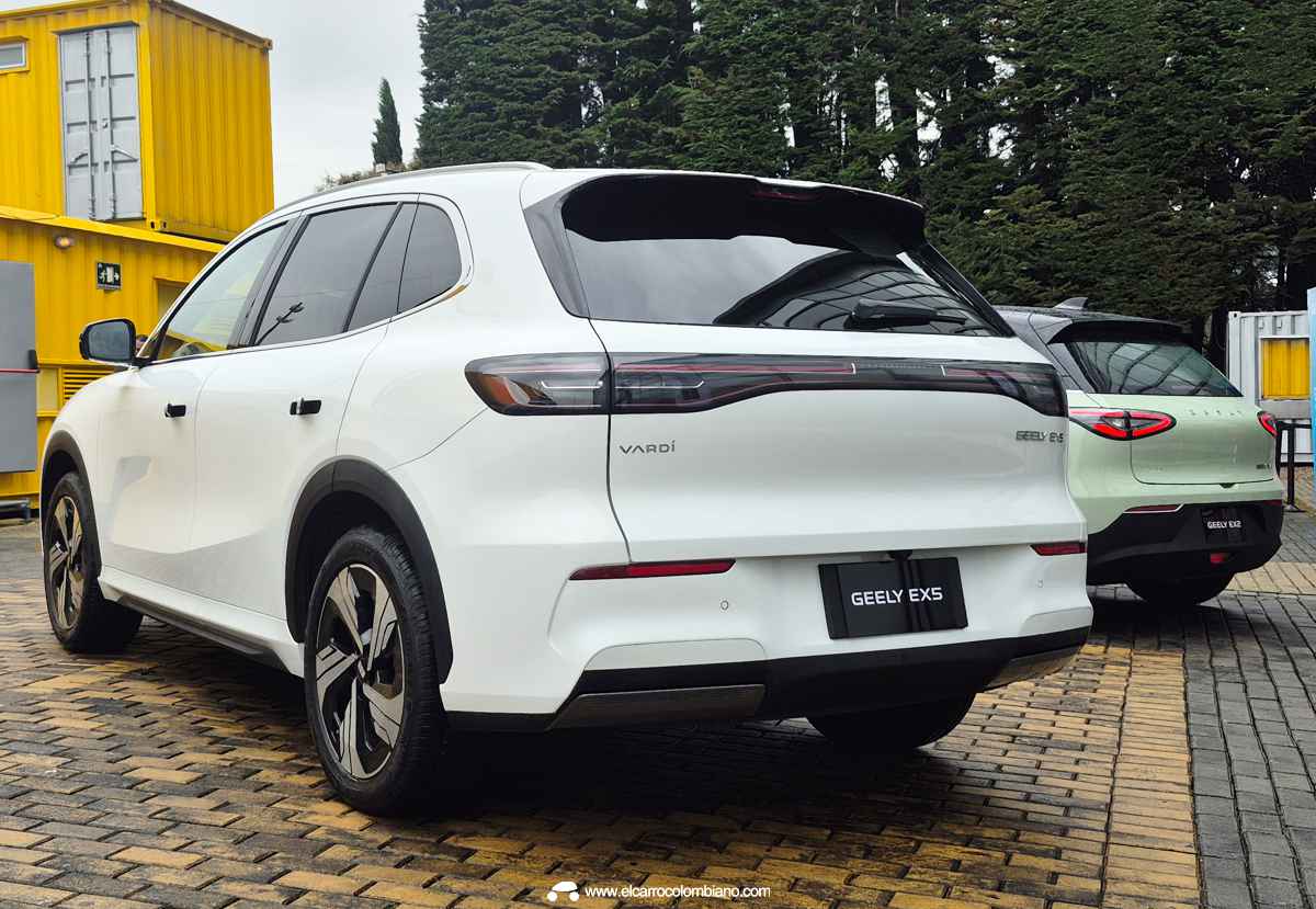 Vista trasera de tres cuartos de la SUV eléctrica Geely EX5 en color blanco. Se destaca la firma lumínica LED continua que recorre todo el portón, el spoiler deportivo superior y los emblemas cromados de Geely y el Grupo Vardí.