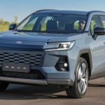 Vista frontal de tres cuartos de la nueva SUV híbrida Toyota RAV4 2026 color azul metálico circulando por una carretera, mostrando su renovada parrilla y faros LED diurnos.