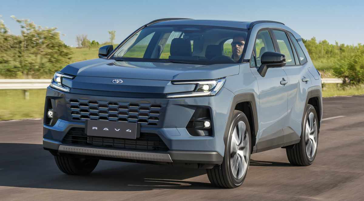 Vista frontal de tres cuartos de la nueva SUV híbrida Toyota RAV4 2026 color azul metálico circulando por una carretera, mostrando su renovada parrilla y faros LED diurnos.