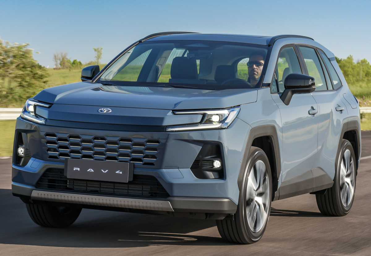 Vista frontal de tres cuartos de la nueva SUV híbrida Toyota RAV4 2026 color azul metálico circulando por una carretera, mostrando su renovada parrilla y faros LED diurnos.