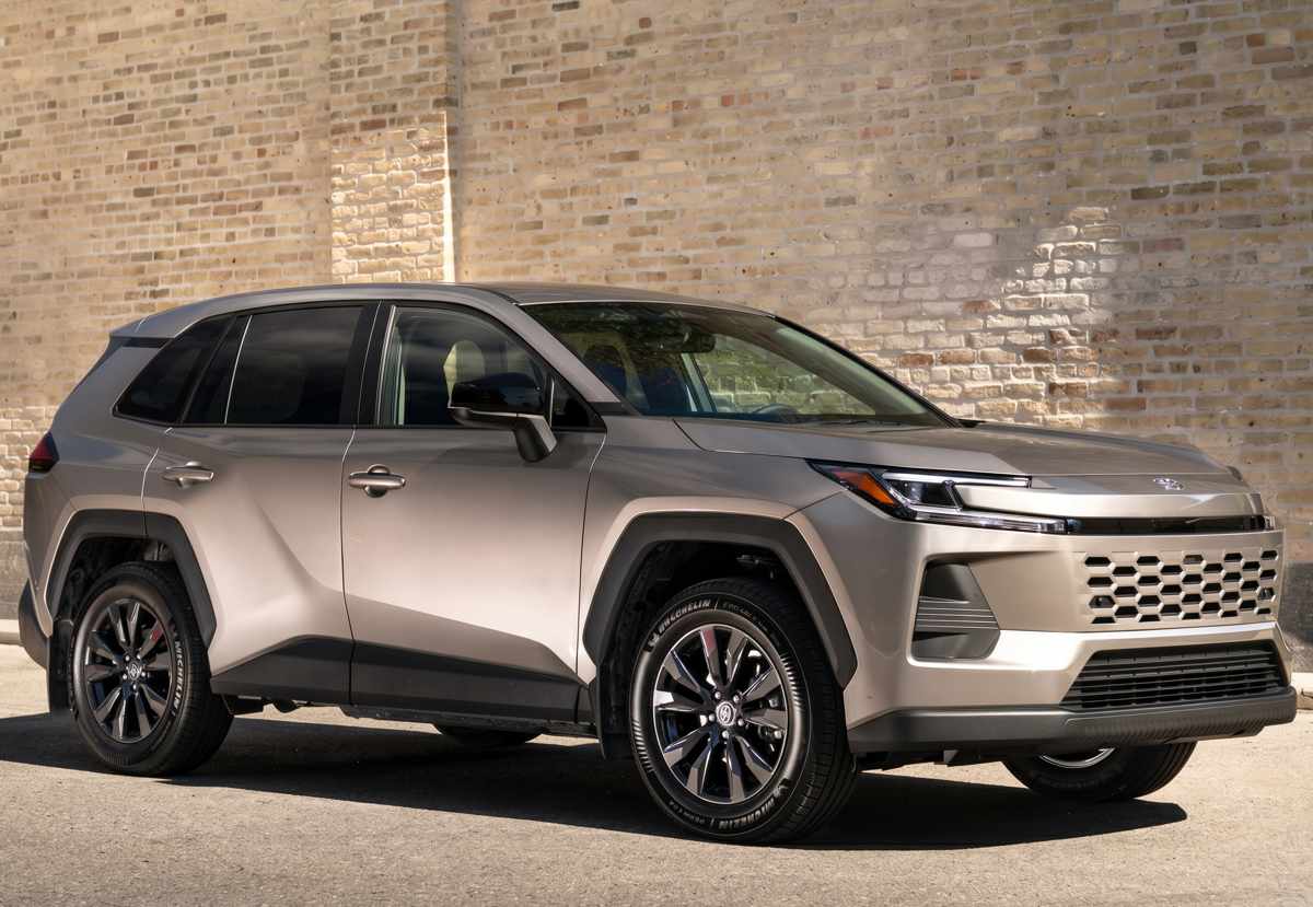 Vista lateral de tres cuartos de la Toyota RAV4 Limited híbrida en color bronce estacionada frente a un muro de ladrillos, destacando sus pasos de rueda trapezoidales y rines bitono de 20 pulgadas.