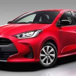 Vista de tres cuartos delantera de un Toyota Yaris híbrido rojo de cuarta generación (versión global), mostrando su parrilla negra con el emblema 'YARIS', faros LED y rines de aleación plateados.