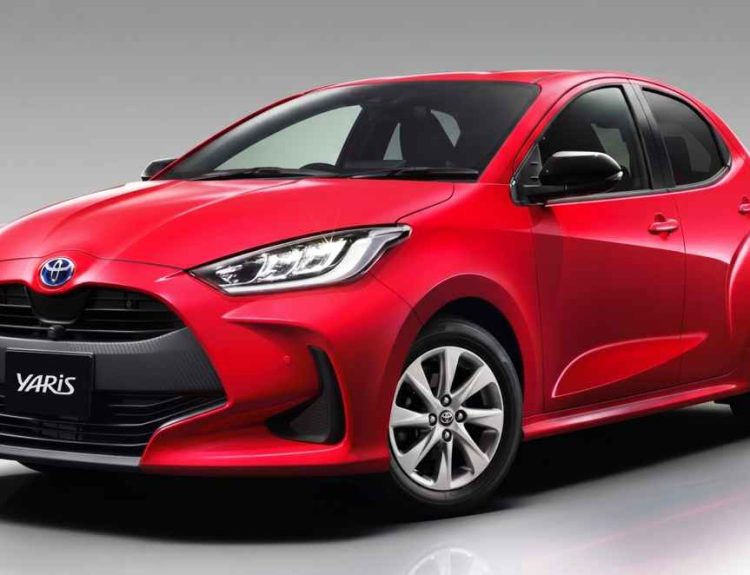 Vista de tres cuartos delantera de un Toyota Yaris híbrido rojo de cuarta generación (versión global), mostrando su parrilla negra con el emblema 'YARIS', faros LED y rines de aleación plateados.