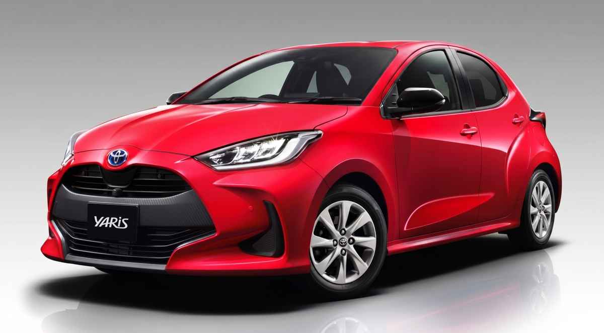 Vista de tres cuartos delantera de un Toyota Yaris híbrido rojo de cuarta generación (versión global), mostrando su parrilla negra con el emblema 'YARIS', faros LED y rines de aleación plateados.