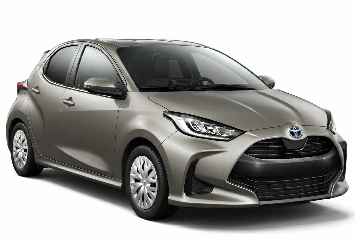 Vista de tres cuartos delantera de un Toyota Yaris híbrido en color beige metalizado (oro champagne) con faros LED y rines de acero con tapacubos.