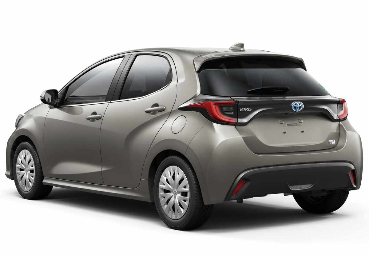 Vista de tres cuartos trasera de un Toyota Yaris híbrido beige metalizado, mostrando sus faros traseros LED, alerón de techo y emblemas 'YARIS' e 'HYBRID'.