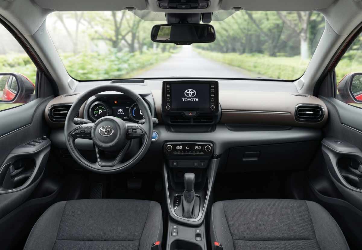 Vista detallada del tablero y la consola central de un Toyota Yaris híbrido, mostrando el volante multifunción, el panel de instrumentos digital, la pantalla táctil central de 9 pulgadas y los controles de climatización.