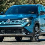 Vista frontal de tres cuartos de la nueva camioneta mediana Renault Boreal en color azul metálico. El vehículo se encuentra estacionado en una zona pavimentada en un día soleado, con árboles verdes de fondo. Se aprecian detalladamente los modernos faros LED en forma de C encendidos, la renovada parrilla frontal con el nuevo logotipo del rombo en el centro y los rines de aleación bitono, mostrando el diseño robusto que llegará a Colombia.