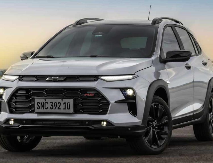 Vista tres cuartos delantera del nuevo crossover Chevrolet Sonic 2027 plateado estacionado, mostrando faros LED principales, luces diurnas superiores divididas, parrilla superior negra con el nuevo logotipo oscuro de la marca, parrilla inferior con emblema 