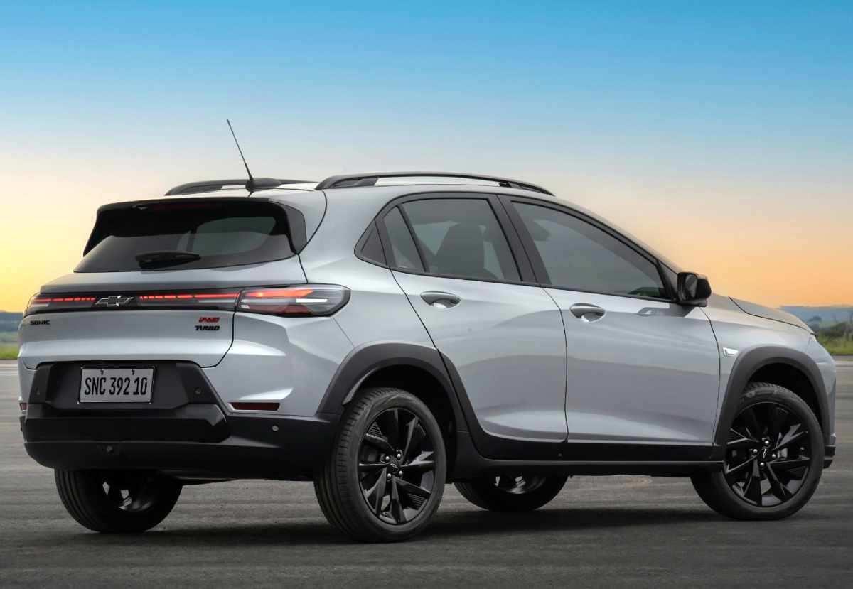 Vista tres cuartos trasera del Chevrolet Sonic 2027 plateado estacionado, mostrando la caída del techo característica de este crossover, barras de techo, rines oscuros de 17 pulgadas, spoiler trasero y el diseño limpio del portón del maletero.