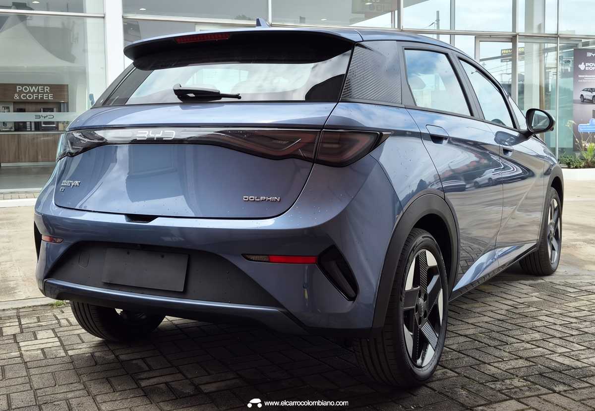 Vista tres cuartos trasera del nuevo BYD Dolphin 2026 color azul estacionado sobre piso adoquinado en exteriores, destacando el diseño limpio de su portón con la inscripción Dolphin, la franja lumínica LED oscurecida, el alerón superior y sus característicos rines bitono aerodinámicos.