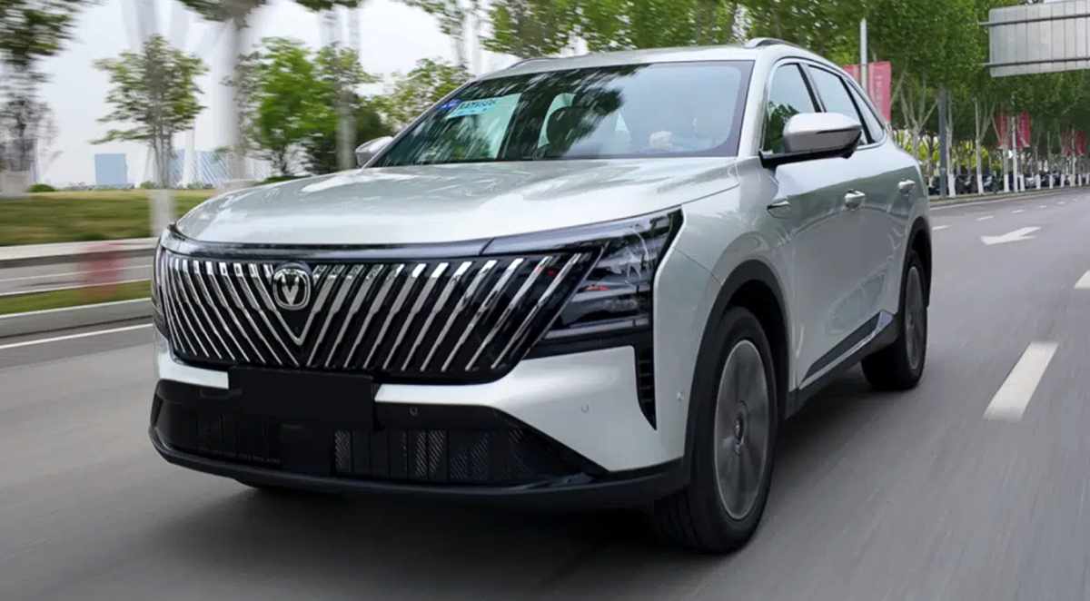 Vista tres cuartos delantera de la nueva Changan CS75 Plus HEV plateada en movimiento sobre una avenida, destacando su enorme parrilla frontal con barras inclinadas.