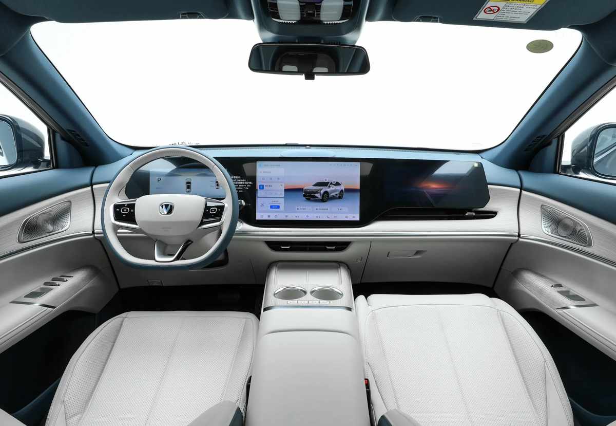 Vista frontal panorámica del interior de la nueva Changan CS75 Plus HEV, exhibiendo el gran módulo continuo de tres pantallas digitales, el volante de tres radios y la consola central despejada con doble cargador inalámbrico.