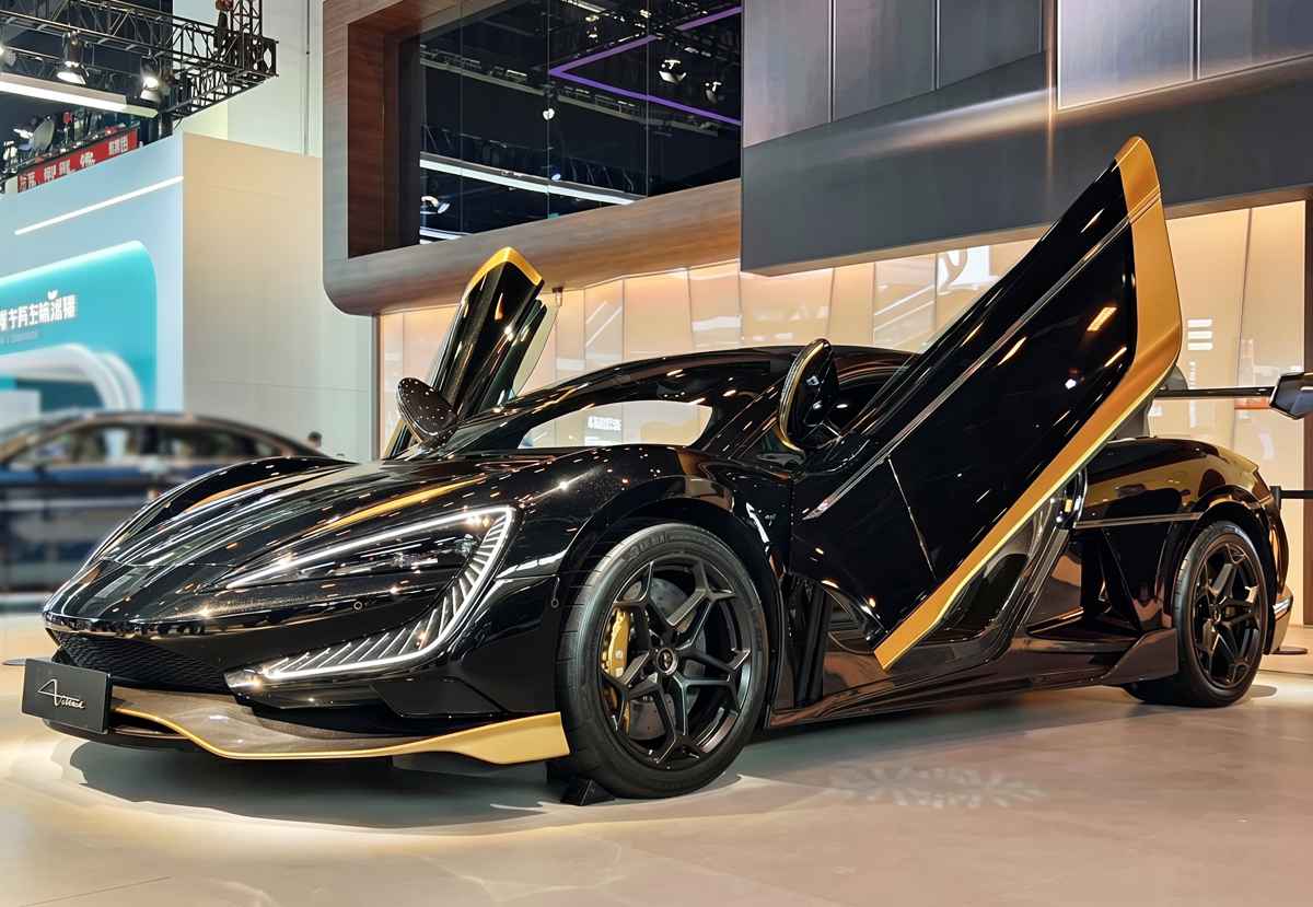Vista lateral de tres cuartos del BYD YangWang U9 Xtreme negro y dorado estacionado en exhibición. Destacan sus enormes llantas oscuras con mordazas de freno doradas, el agresivo diseño aerodinámico de los faldones y la puerta del conductor abierta hacia arriba.