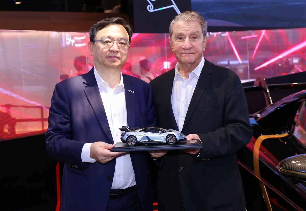 Wang Chuanfu (izquierda), presidente de BYD, posando junto al empresario australiano Nick Politis (derecha) en el Salón de Pekín. Ambos sostienen sonrientes una réplica a escala del hiperdeportivo YangWang U9 Xtreme, simbolizando la entrega del modelo real más caro en la historia de la marca.
