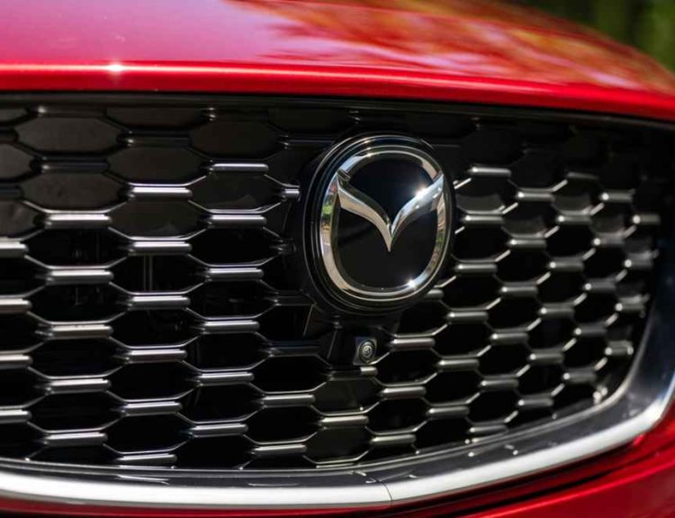Primer plano de la parrilla frontal negra y el logotipo cromado de Mazda en un vehículo color rojo, ilustrando el misterio sobre el reciente registro comercial del nombre CX-40 para un posible nuevo SUV.