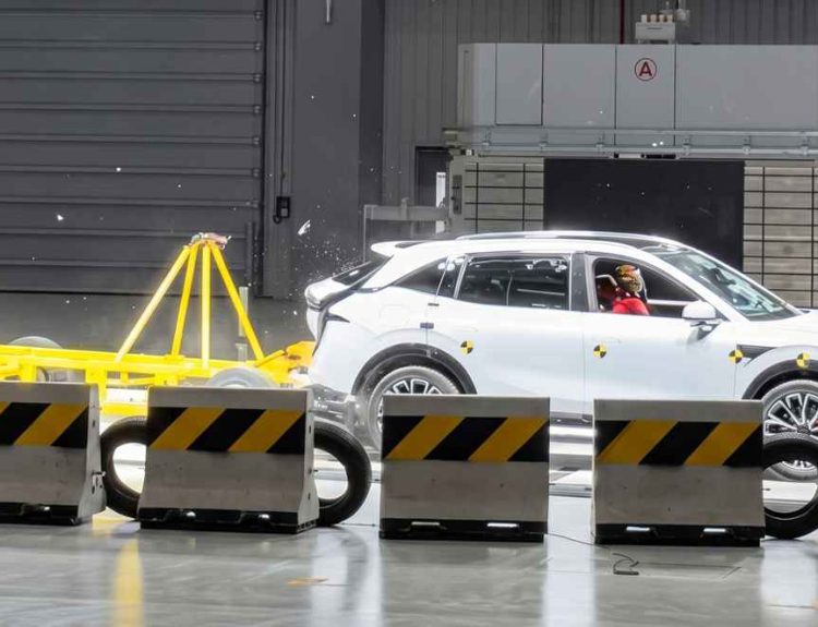 Vista lateral del momento exacto de una prueba de choque en el Centro de Seguridad de Geely. Una plataforma móvil amarilla impacta violentamente la parte trasera de una camioneta Zeekr 7X color blanco, con un maniquí de pruebas visible al volante.