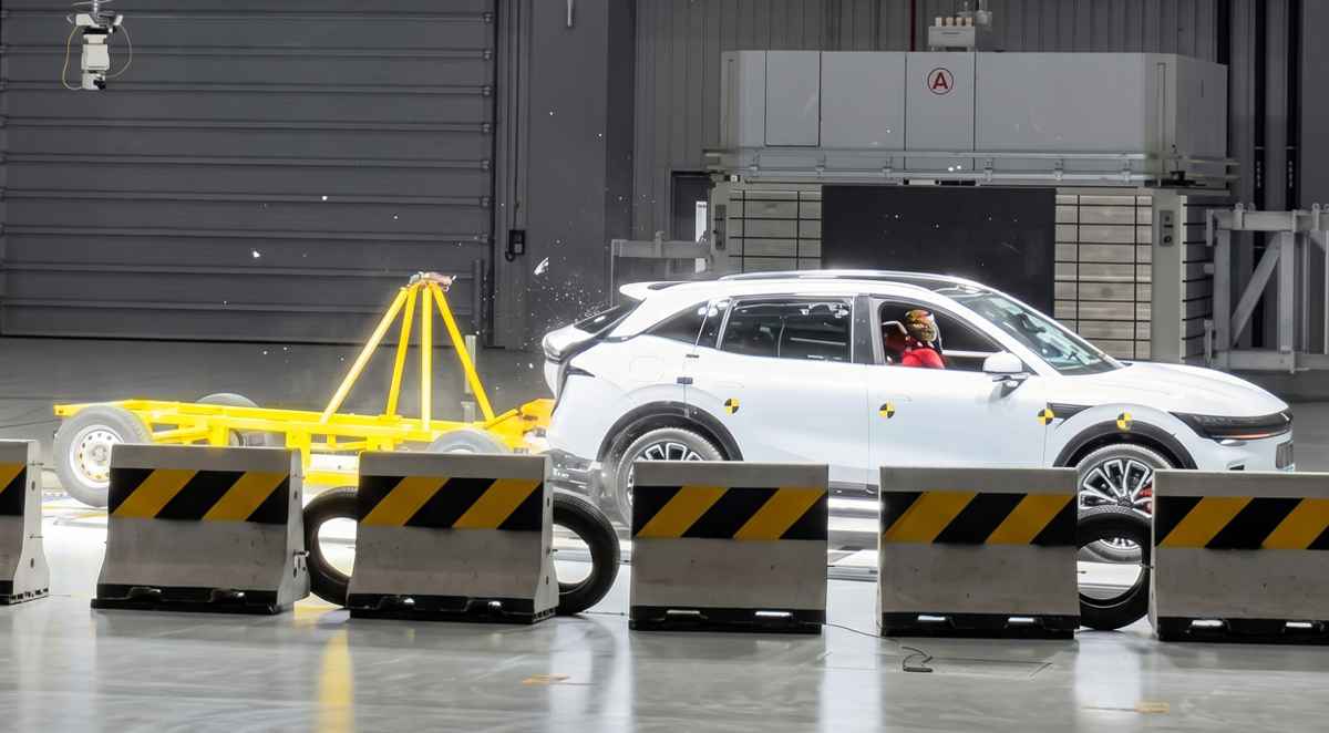 Vista lateral del momento exacto de una prueba de choque en el Centro de Seguridad de Geely. Una plataforma móvil amarilla impacta violentamente la parte trasera de una camioneta Zeekr 7X color blanco, con un maniquí de pruebas visible al volante.