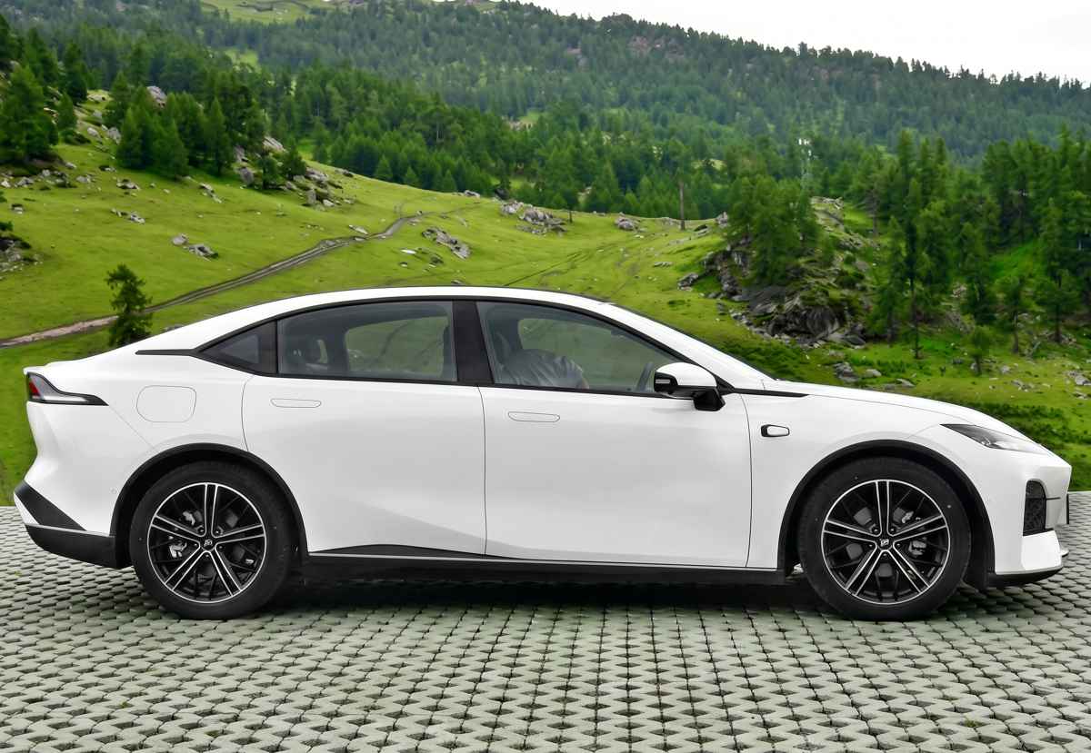 Perfil lateral del sedán Deepal SL03 color blanco estacionado frente a un verde paisaje montañoso. Se aprecian sus líneas de diseño fluidas, manijas de puertas enrasadas en la carrocería, rines aerodinámicos en bitono y una suave caída de techo tipo fastback.