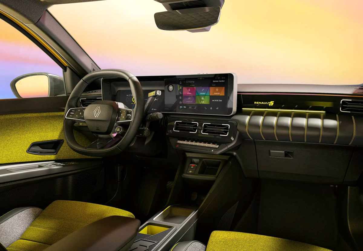 Vista interior de la cabina del Renault 5 E-Tech eléctrico. Destaca su panel de instrumentos digital dual, el volante multifunción, el selector de marchas ubicado en la columna de dirección y los llamativos asientos con tapicería de textura gruesa en color amarillo y gris.