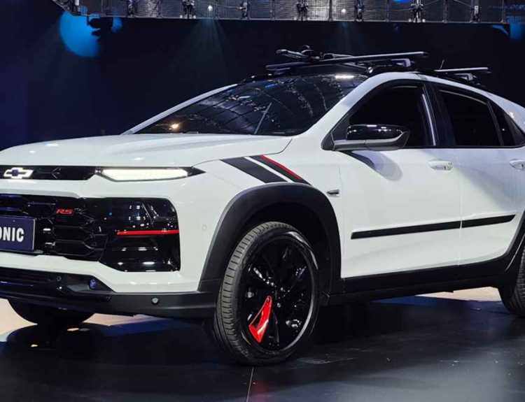 Vista en tres cuartos delantero del nuevo Chevrolet Sonic 2027 versión RS color blanco, durante su presentación oficial. Destacan sus rines negros con detalles en rojo, el frontal agresivo con faros divididos y molduras plásticas oscuras que acentúan su nuevo formato SUV compacto.