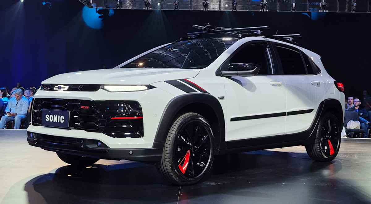 Vista en tres cuartos delantero del nuevo Chevrolet Sonic 2027 versión RS color blanco, durante su presentación oficial. Destacan sus rines negros con detalles en rojo, el frontal agresivo con faros divididos y molduras plásticas oscuras que acentúan su nuevo formato SUV compacto.